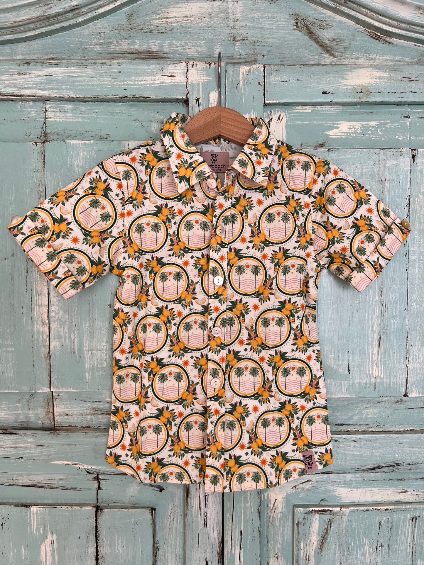 short-sleeves organic cotton button-up shirt for kids with a tropical-inspired print featuring palm trees and lemons motifs. Designed with a classic collar and relaxed fit for breathable comfort.