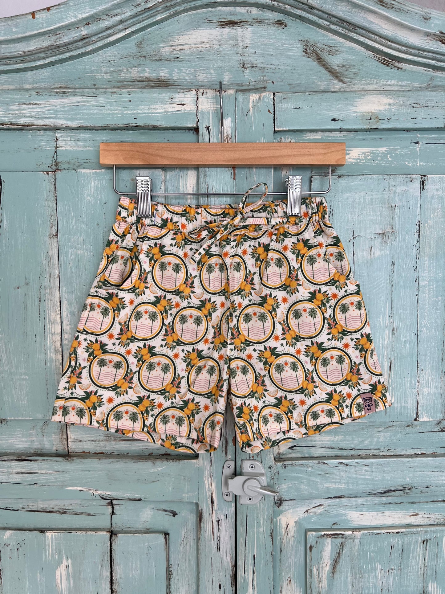 organic cotton shorts for kids age 2 to 9 years old, soft white base with palms and lemon and leaf print, relaxed fit, elastic waistband, and an adjustable drawstring.