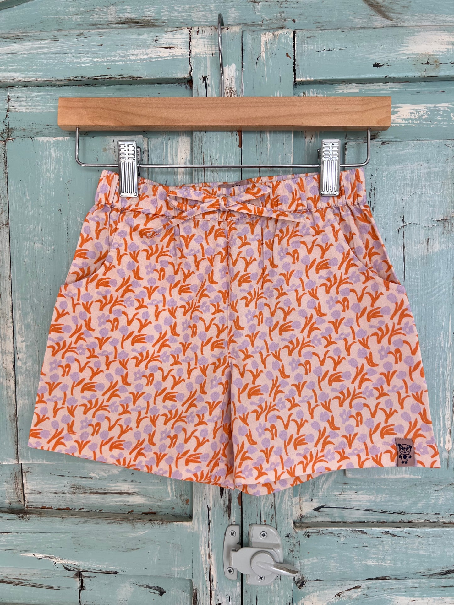 organic cotton shorts for kids age 2 to 9 years old, soft pink base with tulips and leaf and leaf print, orange and violet colors, relaxed fit, elastic waistband, and an adjustable drawstring.