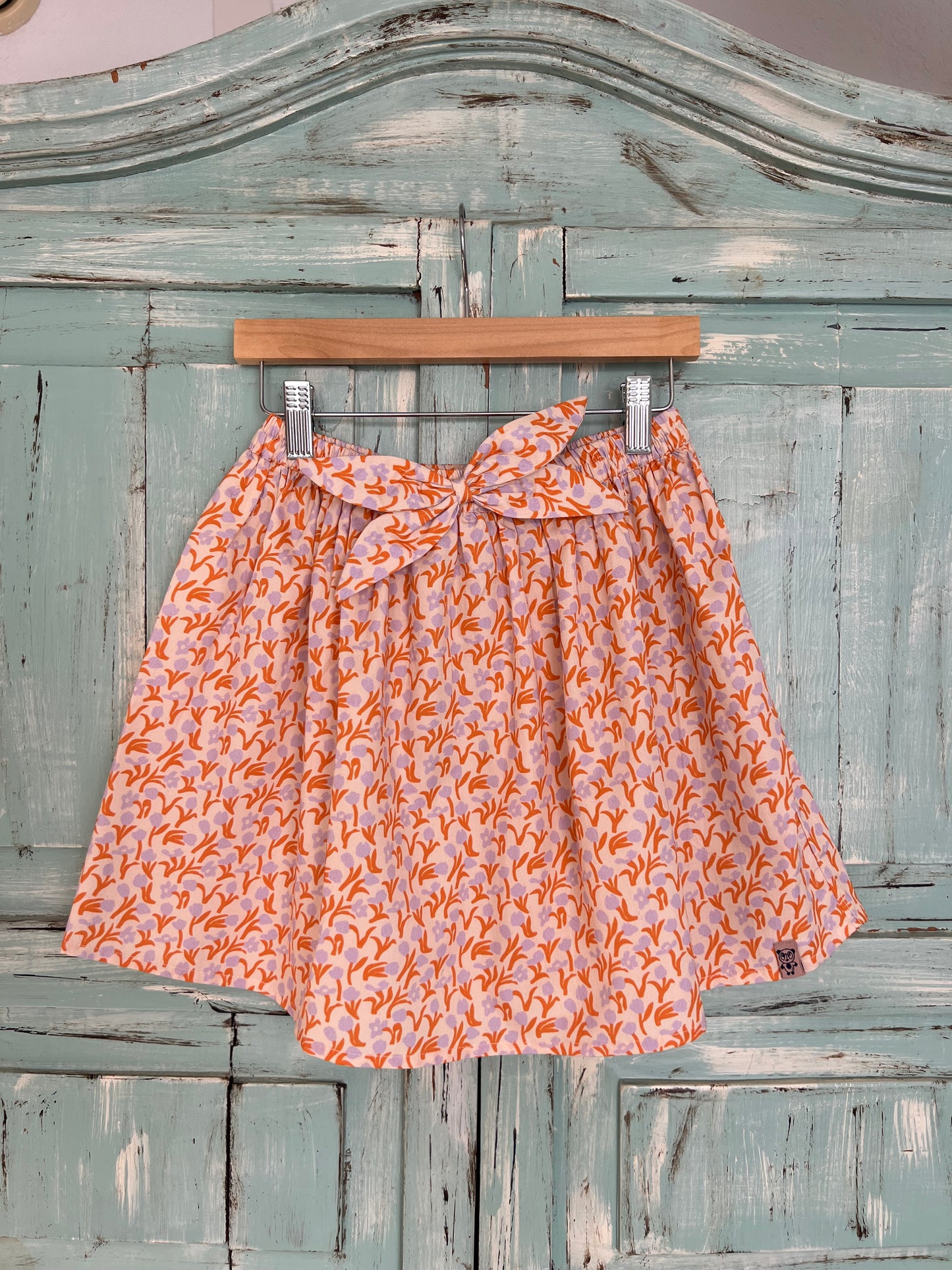 soft organic cotton skirt for girls age 2 to 8 years old. flowery print with a soft pink base and orange and violet tulips, featuring a wavy style,flowy design, elastic waistband and matching fabric decorative bow.