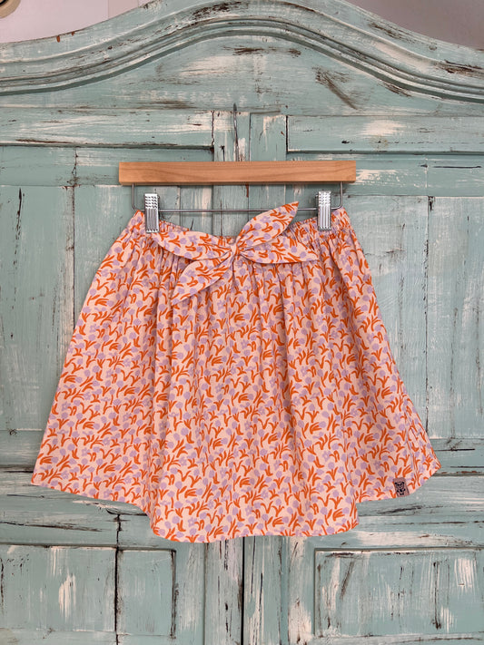 soft organic cotton skirt for girls age 2 to 8 years old. flowery print with a soft pink base and orange and violet tulips, featuring a wavy style,flowy design, elastic waistband and matching fabric decorative bow.