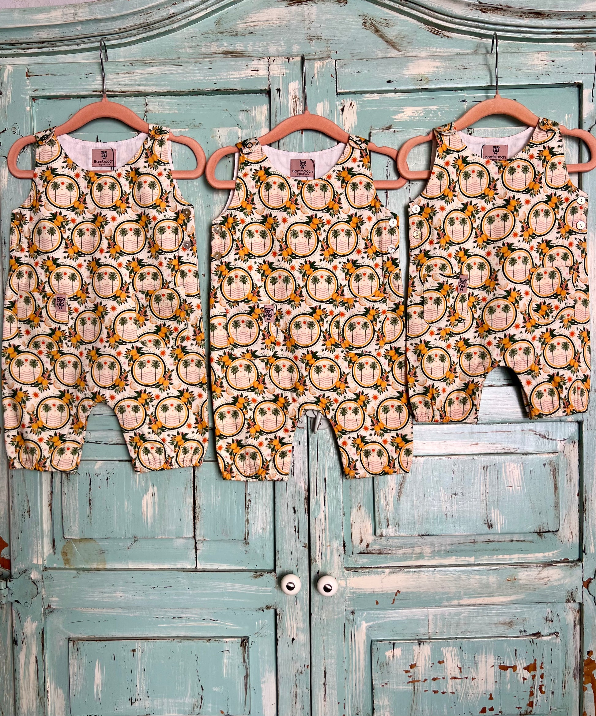 Three baby rompers with owl pattern on hangers against a rustic wooden door.