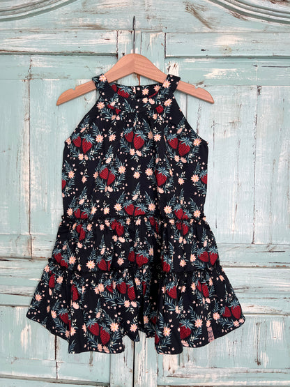 Sleeveless organic cotton dress for girls age 2 to 7, with a black background and a vibrant strawberry floral print.
Features high neckline and tiered ruffle skirt for a playful flow look.Fabric button on the back neck line for easy fit