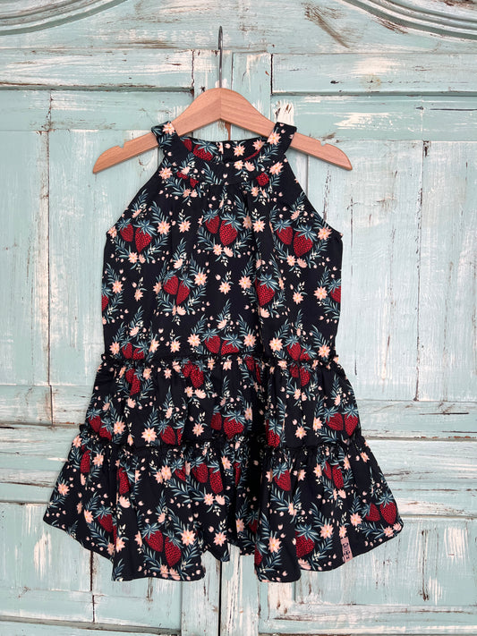 Sleeveless organic cotton dress for girls age 2 to 7, with a black background and a vibrant strawberry floral print.
Features high neckline and tiered ruffle skirt for a playful flow look.Fabric button on the back neck line for easy fit