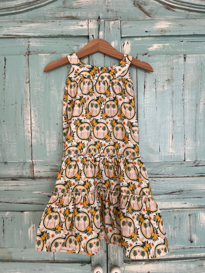 Sleeveless organic cotton dress for girls age 2 to 7, with a soft white background and a vibrant palms and lemons floral print.
Features high neckline and tiered ruffle skirt for a playful flow look.Fabric button on the back neck line for easy fit