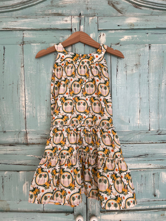 Sleeveless organic cotton dress for girls age 2 to 7, with a soft white background and a vibrant palms and lemons floral print.
Features high neckline and tiered ruffle skirt for a playful flow look.Fabric button on the back neck line for easy fit