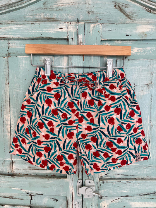 organic cotton shorts for kids age 2 to 9 years old, soft pink base with pomegranate and leaf print, relaxed fit, elastic waistband, and an adjustable drawstring.